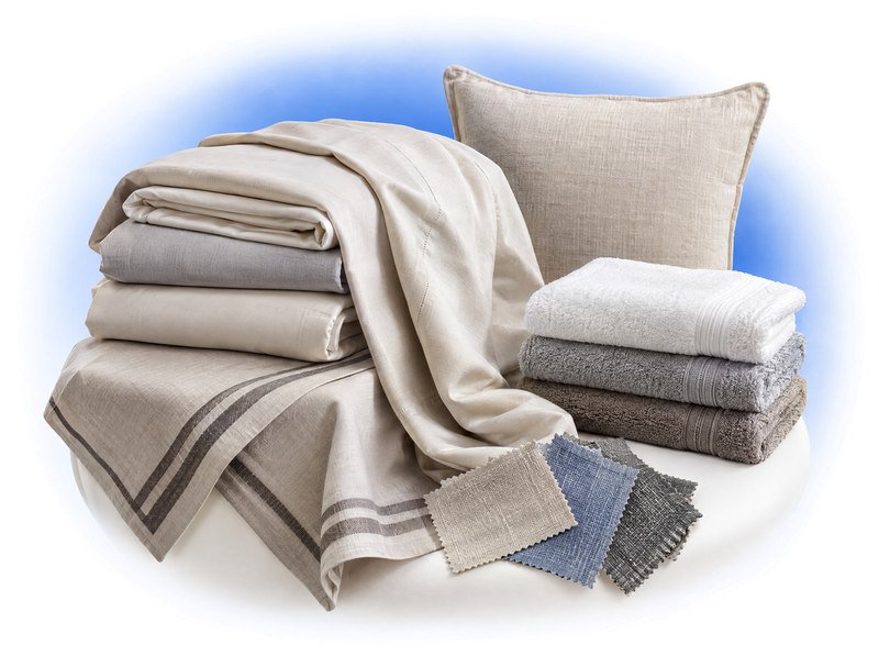 Layered bed linen, towels, a cushion and woven fabric samples showing different textures